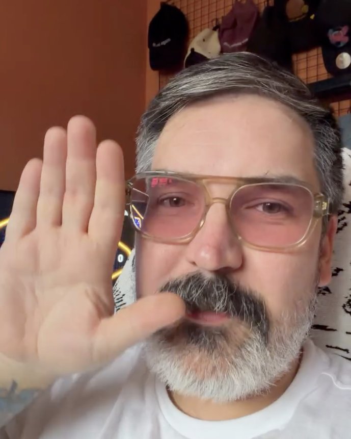 Gary waving at the camera in pink-tinted glasses