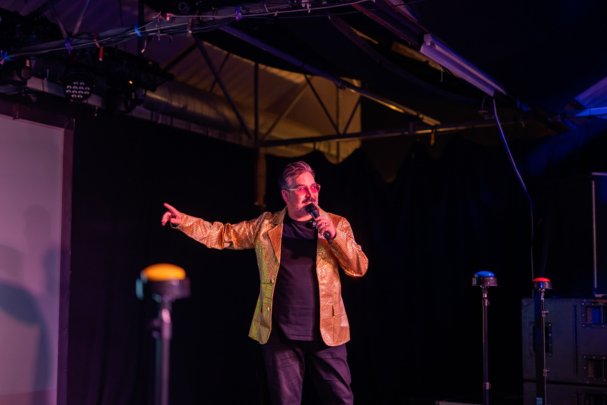 Gary on stage in a gold sequin jacket, microphone in hand, pointing out at the crowd.